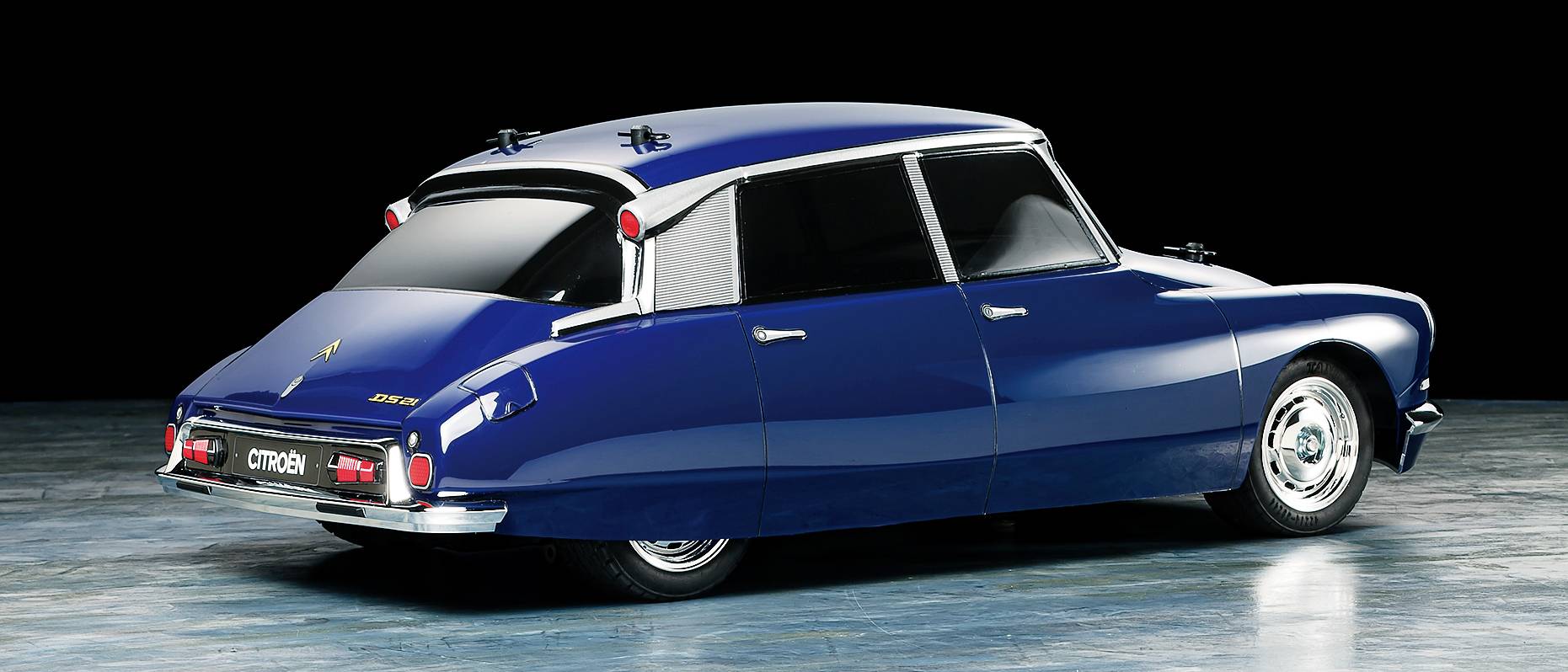 Une Citroën DS bleue des années 1960, photographiée de dos dans un studio. La voiture présente un design aérodynamique et des détails chromés.
