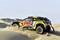 Une voiture de rallye jaune arborant les logos de 'Bardahl' et 'Red Bull' traverse un paysage désertique parsemé de hautes dunes de sable.