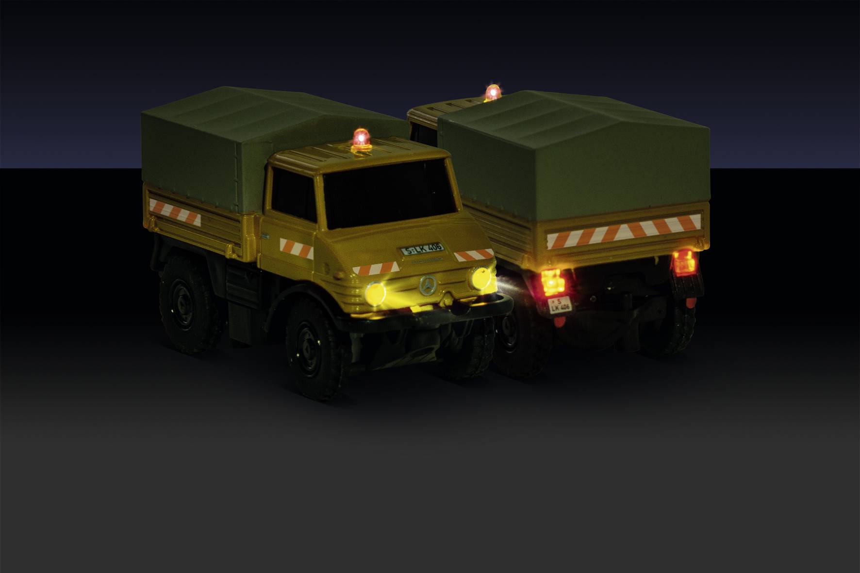 Deux camions-jouets jaunes avec des feux oranges et des bâches vertes sont disposés sur un fond sombre. Ils sont visibles de l'arrière et de l'avant.