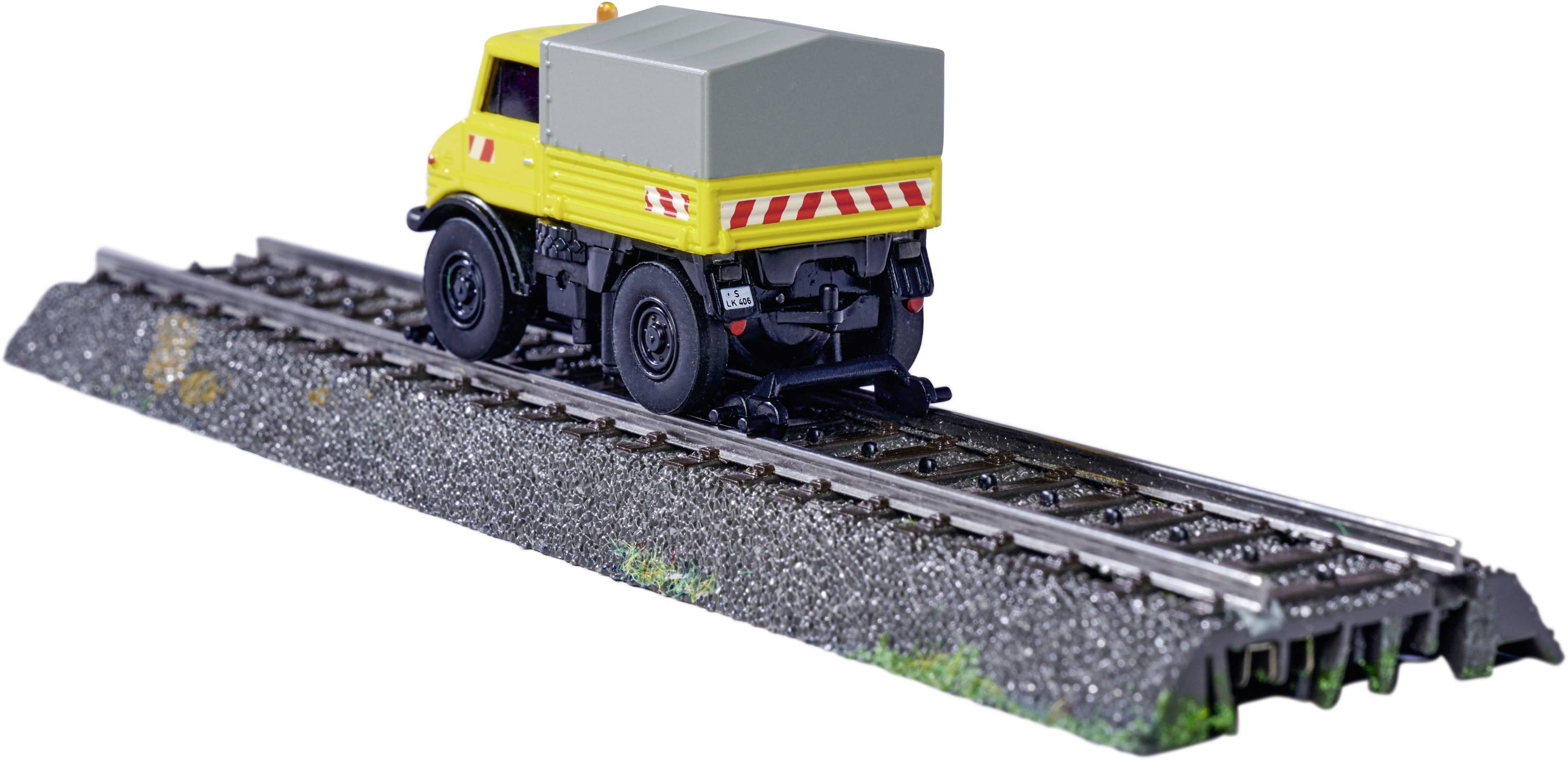 Un camion jaune roule sur des rails de chemin de fer. Le véhicule est placé sur un modèle de voie ferrée et semble équipé pour l'entretien des voies.