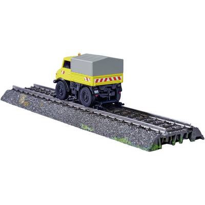 Un camion jaune roule sur des rails de chemin de fer. Le véhicule est placé sur un modèle de voie ferrée et semble équipé pour l'entretien des voies.