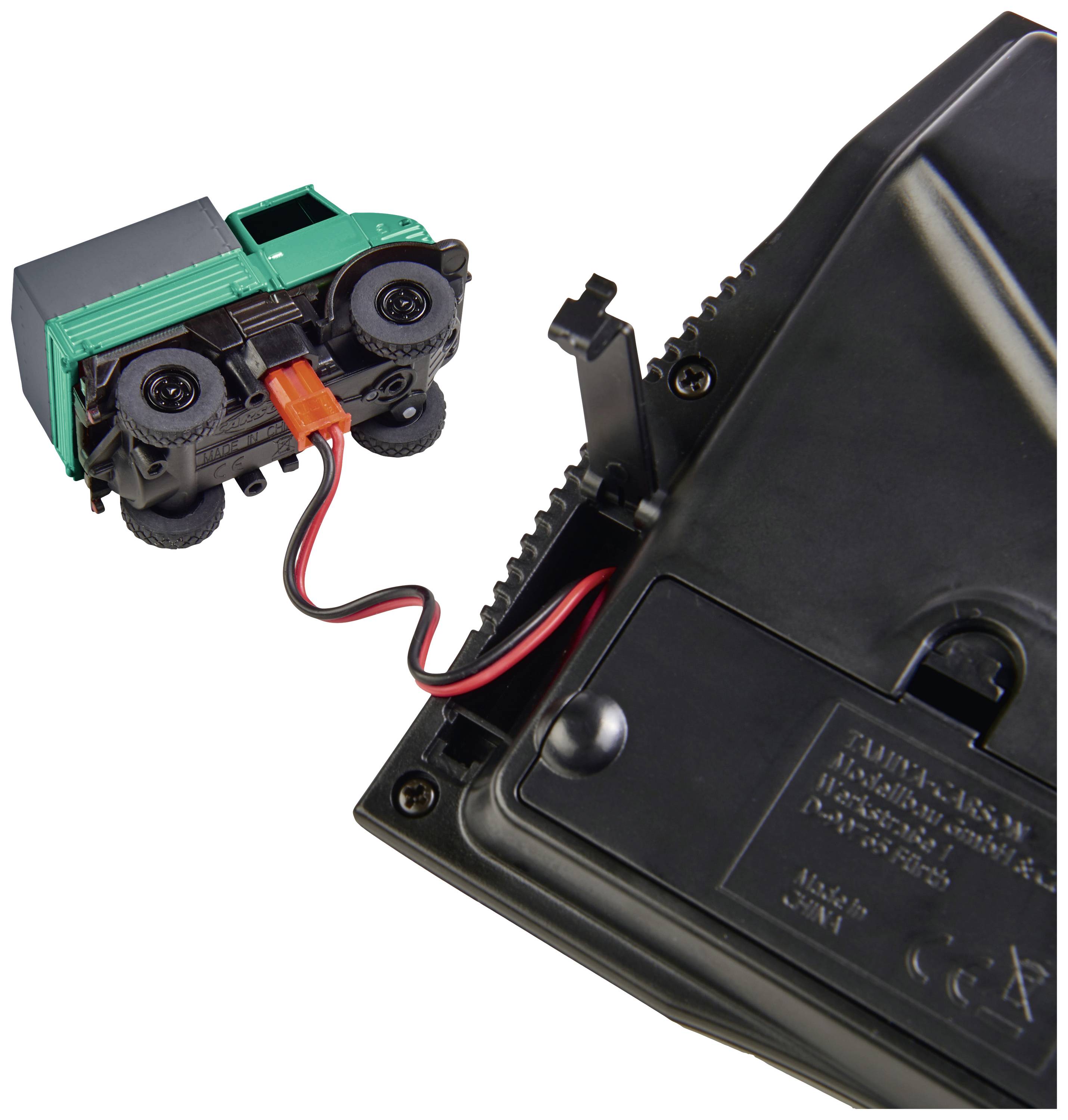 Le camion-jouet est connecté à une télécommande noire par un câble. L'arrière de la télécommande présente des détails techniques.