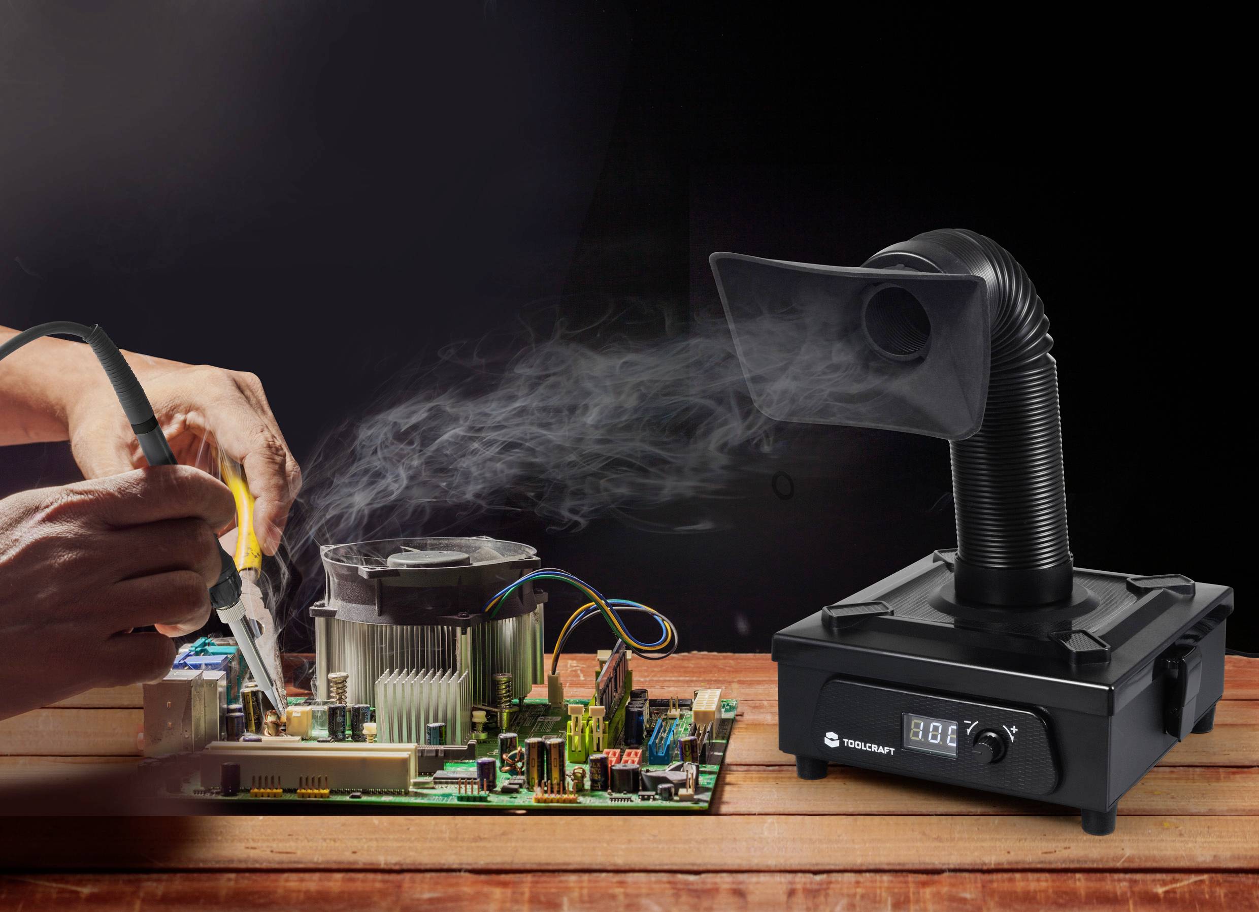 'Une personne soude sur une carte de circuit imprimé tandis qu'un extracteur de fumée aspire la fumée.'