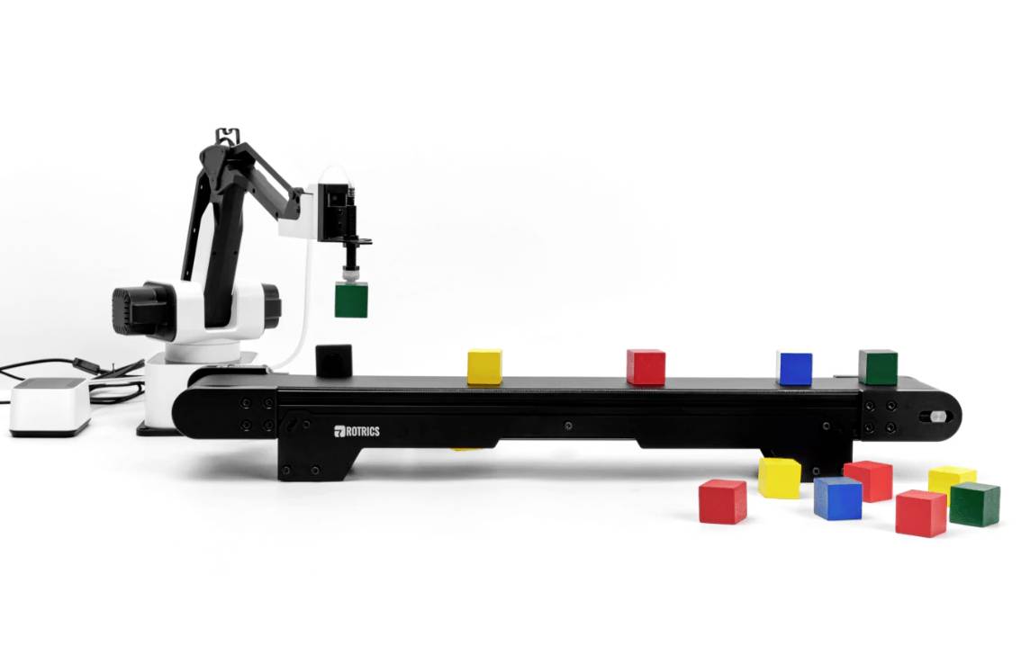 Un bras robotique place des cubes colorés sur un tapis roulant. D'autres cubes multicolores sont disposés sur le sol.