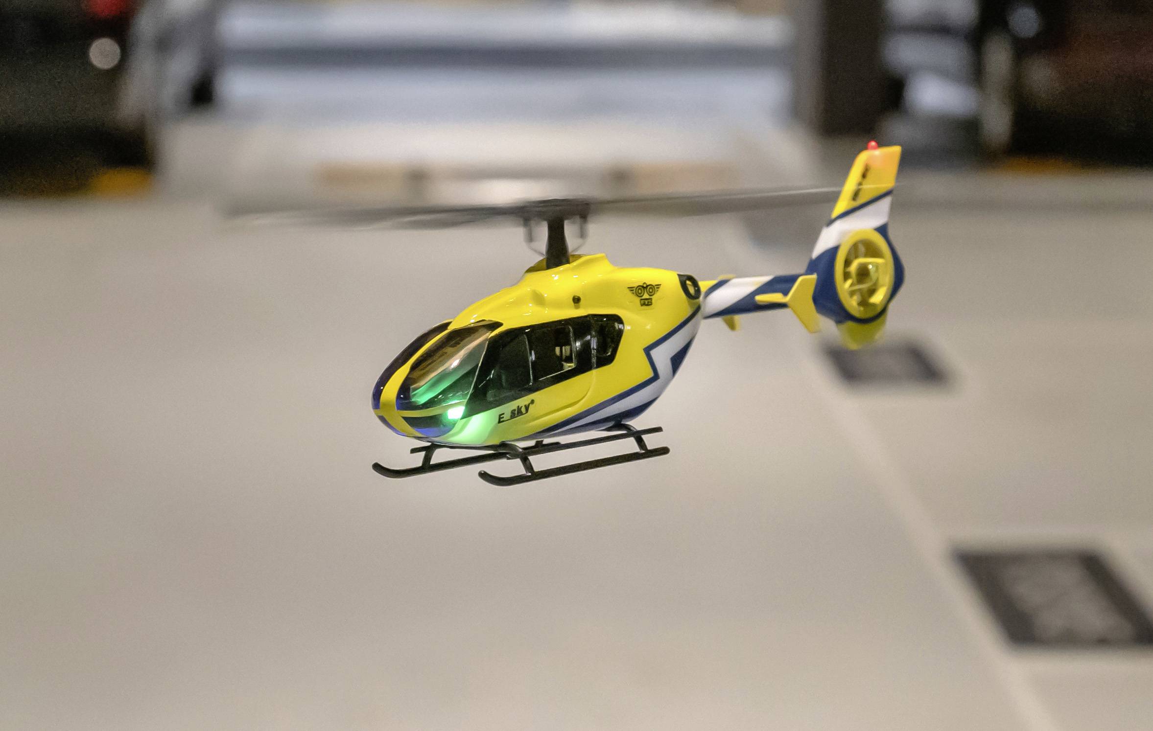 Un petit hélicoptère télécommandé jaune vole avec une lumière verte brillante à l'intérieur d'un espace.