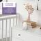 Une chambre de bébé avec un babyphone blanc posé sur une commode, à côté de deux livres et d'un vase contenant des herbes séchées.