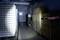 Dans un entrepôt sombre, une personne braque une lampe de poche sur des cartons empilés qui délimitent un passage étroit.