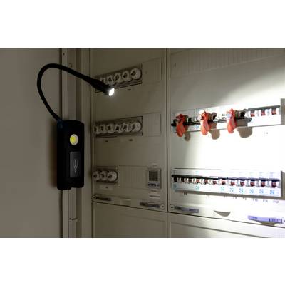 Dans une pièce sombre, une lampe portative éclaire un coffret électrique qui montre des fusibles et des interrupteurs.