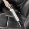 Une personne nettoie un siège de voiture avec un aspirateur à main blanc. Le siège est en cuir noir.