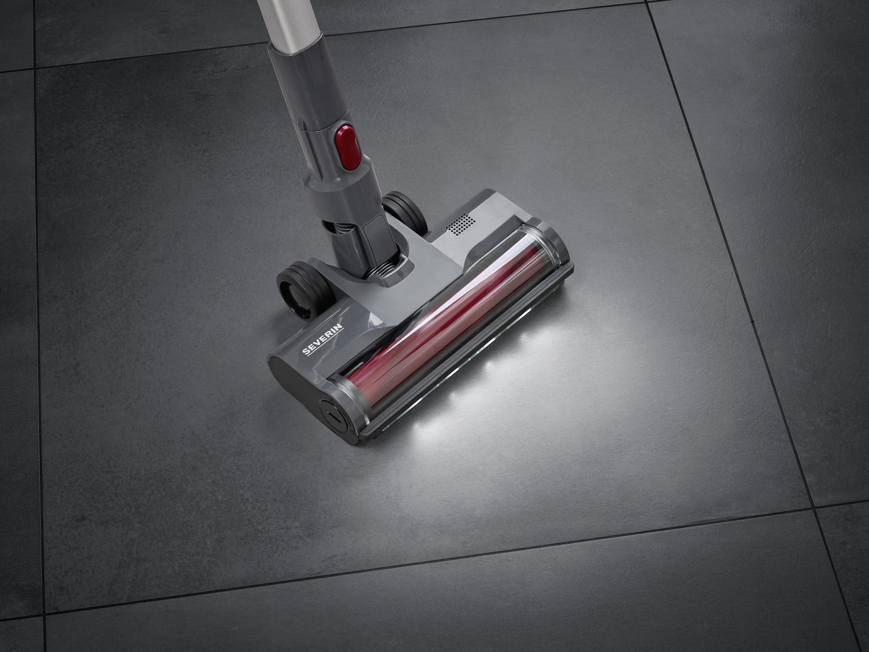 Un aspirateur doté de lumières LED nettoie des carreaux sombres, le sol révèle une zone brillante et propre.