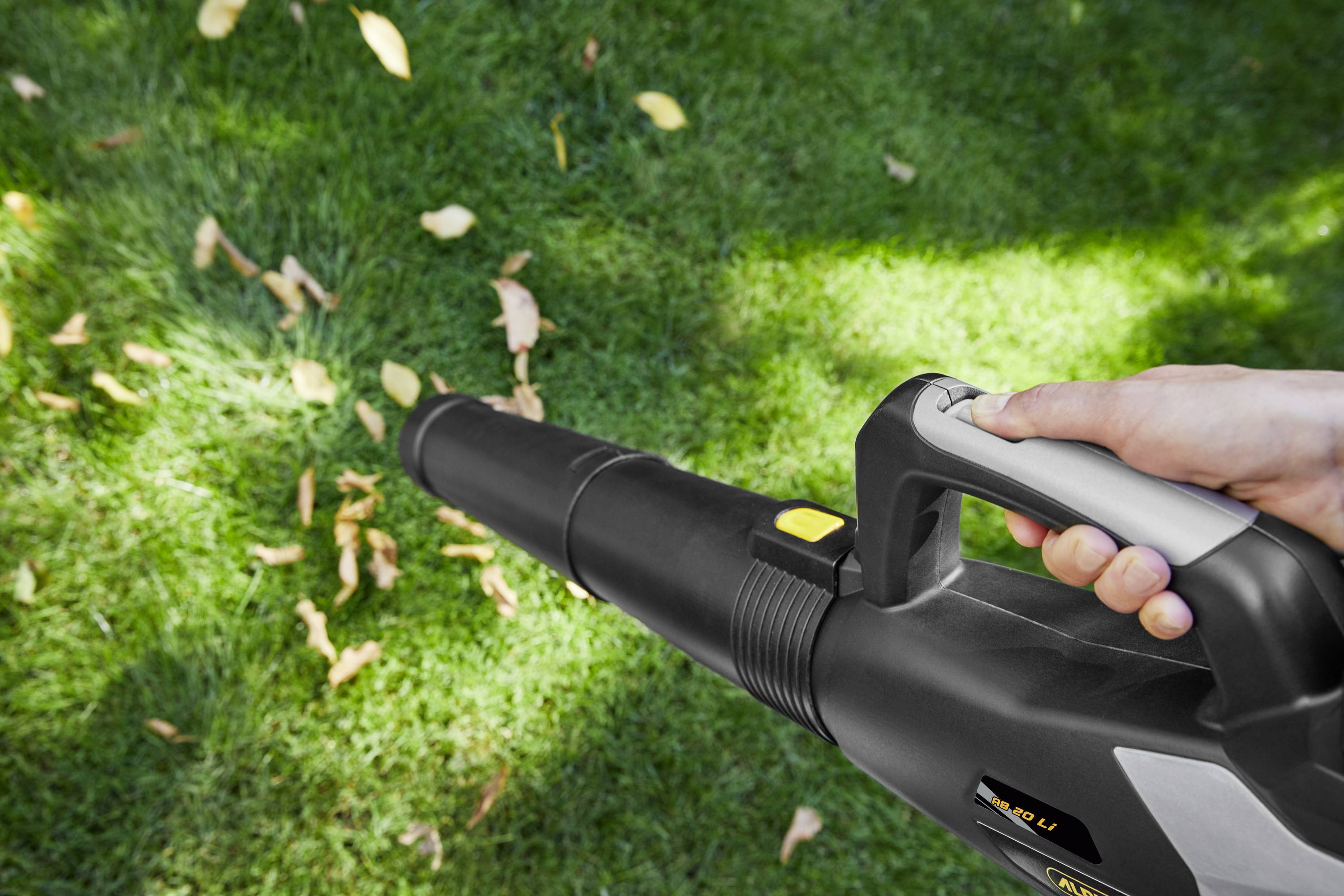 Une personne tient un souffleur de feuilles et souffle des feuilles d'automne d'une surface de pelouse verte.