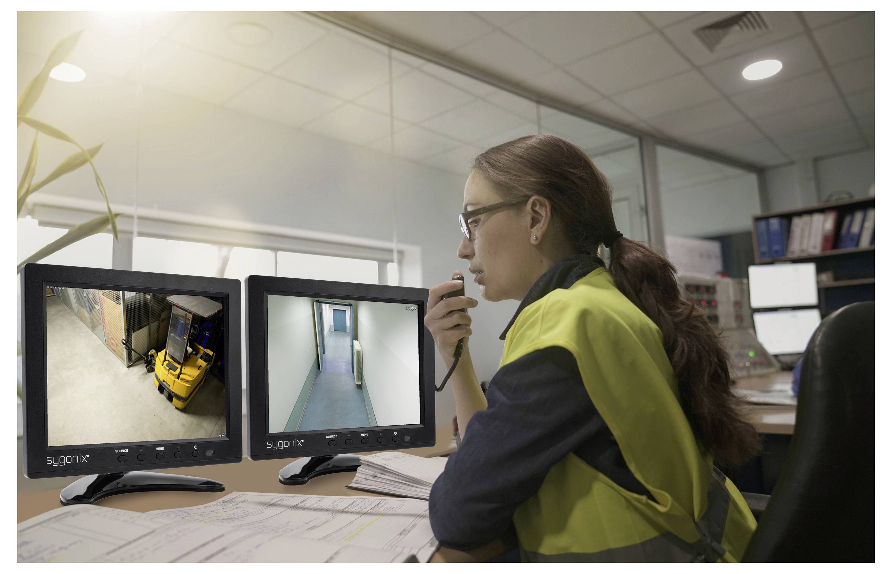 Un opérateur de sécurité dans une salle de contrôle surveille deux écrans de vidéosurveillance, l'un montrant un chariot élévateur dans un entrepôt et l'autre un couloir vide.