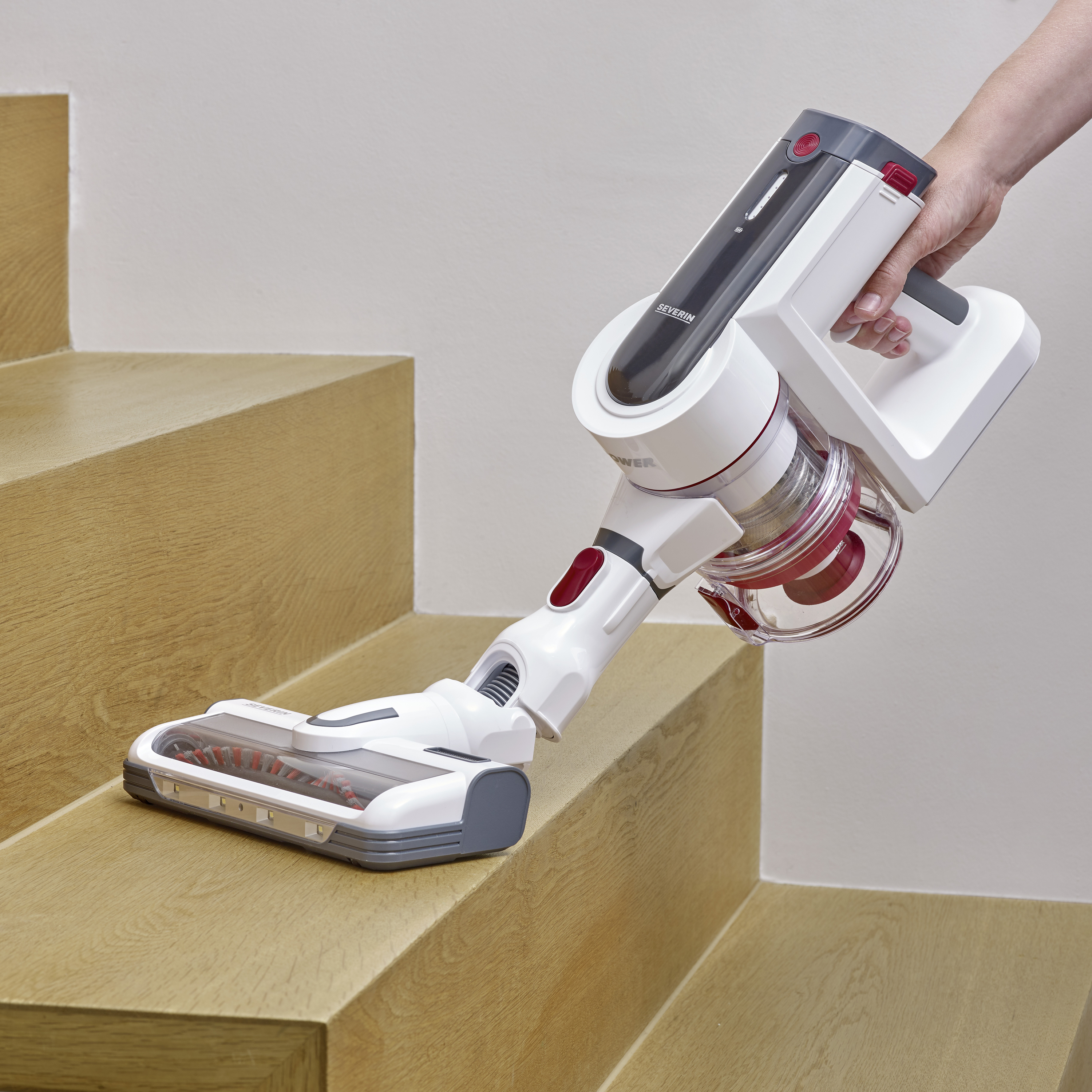 Une personne nettoie des marches d'escalier à l'aide d'un aspirateur sans fil portable sur un escalier en bois. L'accent est mis sur l'efficacité et l'ergonomie.