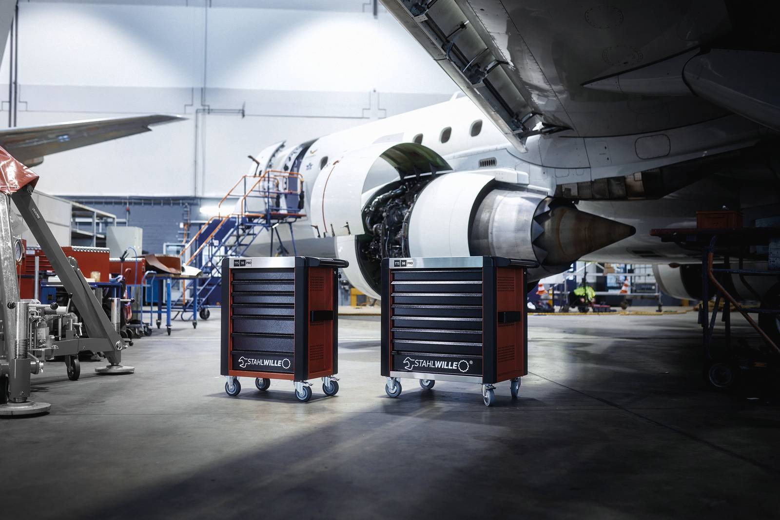 Atelier avec deux armoires à outils mobiles devant un moteur d'avion dans un grand hangar. Technologie et maintenance au premier plan.