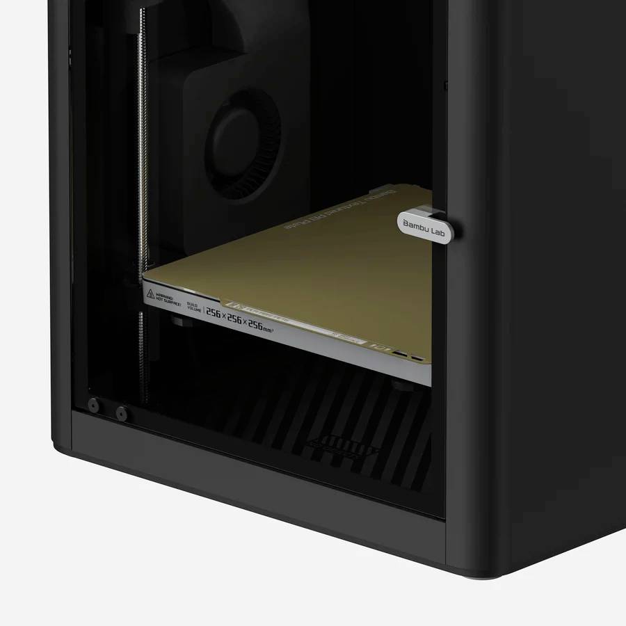 Imprimante 3D noire à boîtier ouvert, avec un détail sur la gauche montrant la plateforme d'impression et la buse à l'intérieur.
