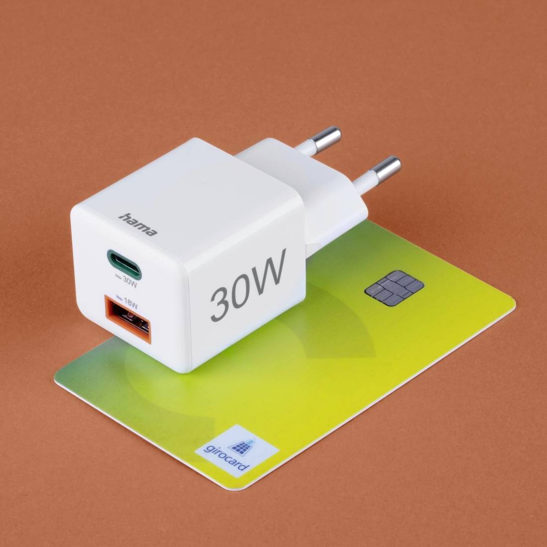 Un chargeur blanc 'hama' de 30W est posé sur une carte bancaire. Il dispose d'un port USB-C, d'un port USB-A et d'une fiche européenne.