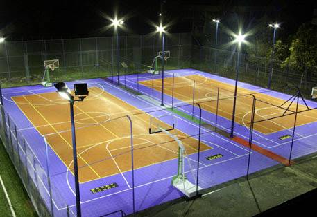 Un terrain de basketball bien éclairé à l'extérieur la nuit, avec deux terrains, entouré d'une clôture.
