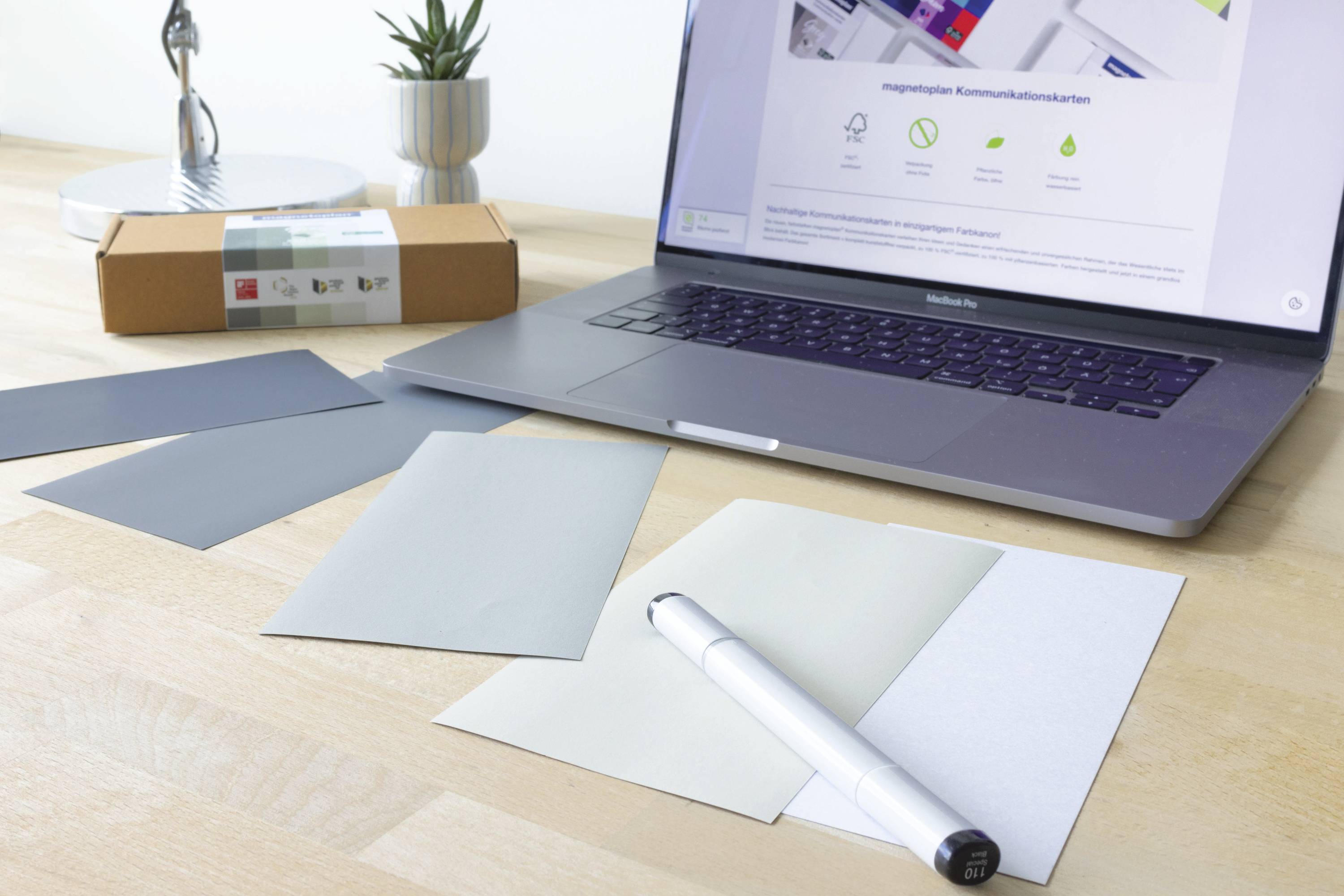 Un ordinateur portable affiche un site web sur la communication moderne ; à côté, des nuanciers et un stylo sont posés sur un bureau.