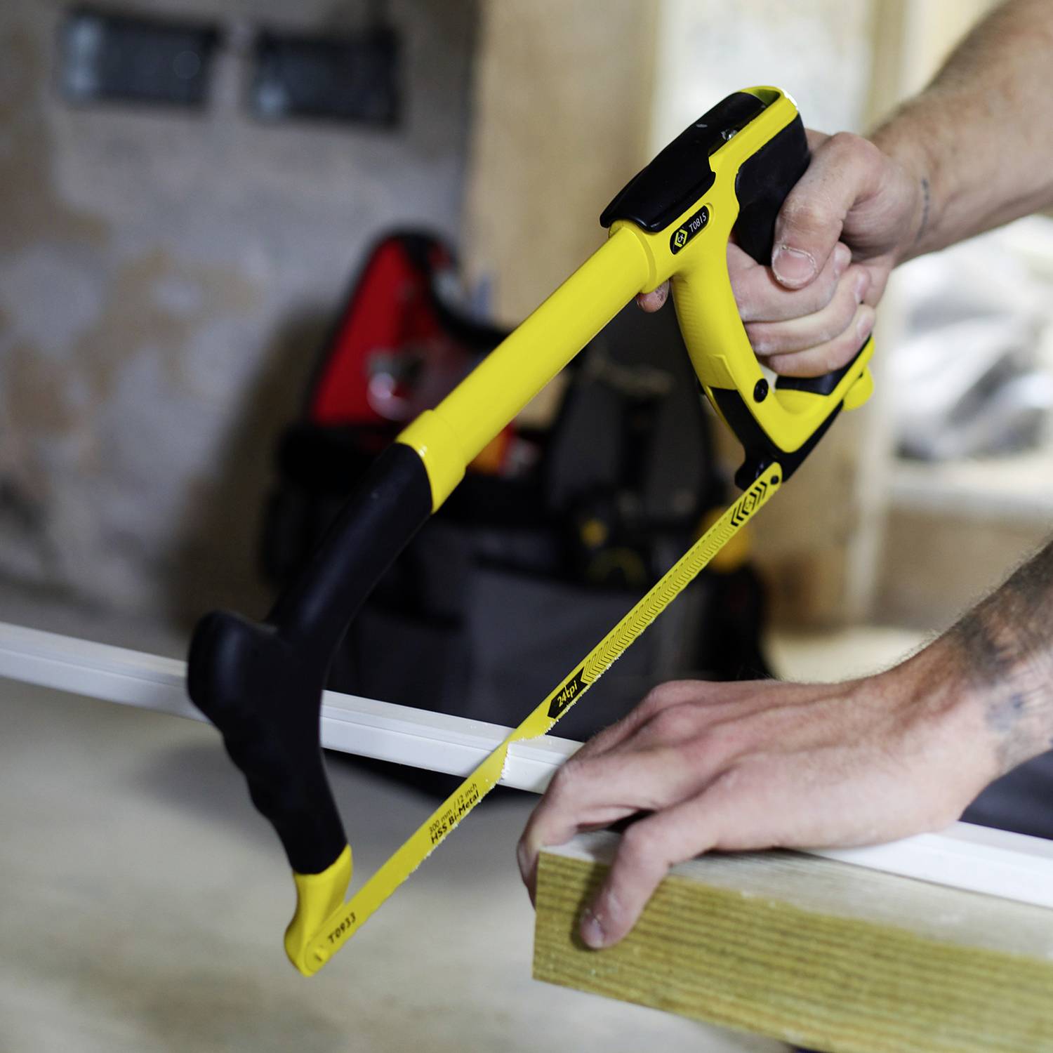 Un utilisateur d'outils scie une planche en bois avec une scie à archet jaune. Expression concentrée, arrière-plan flou.