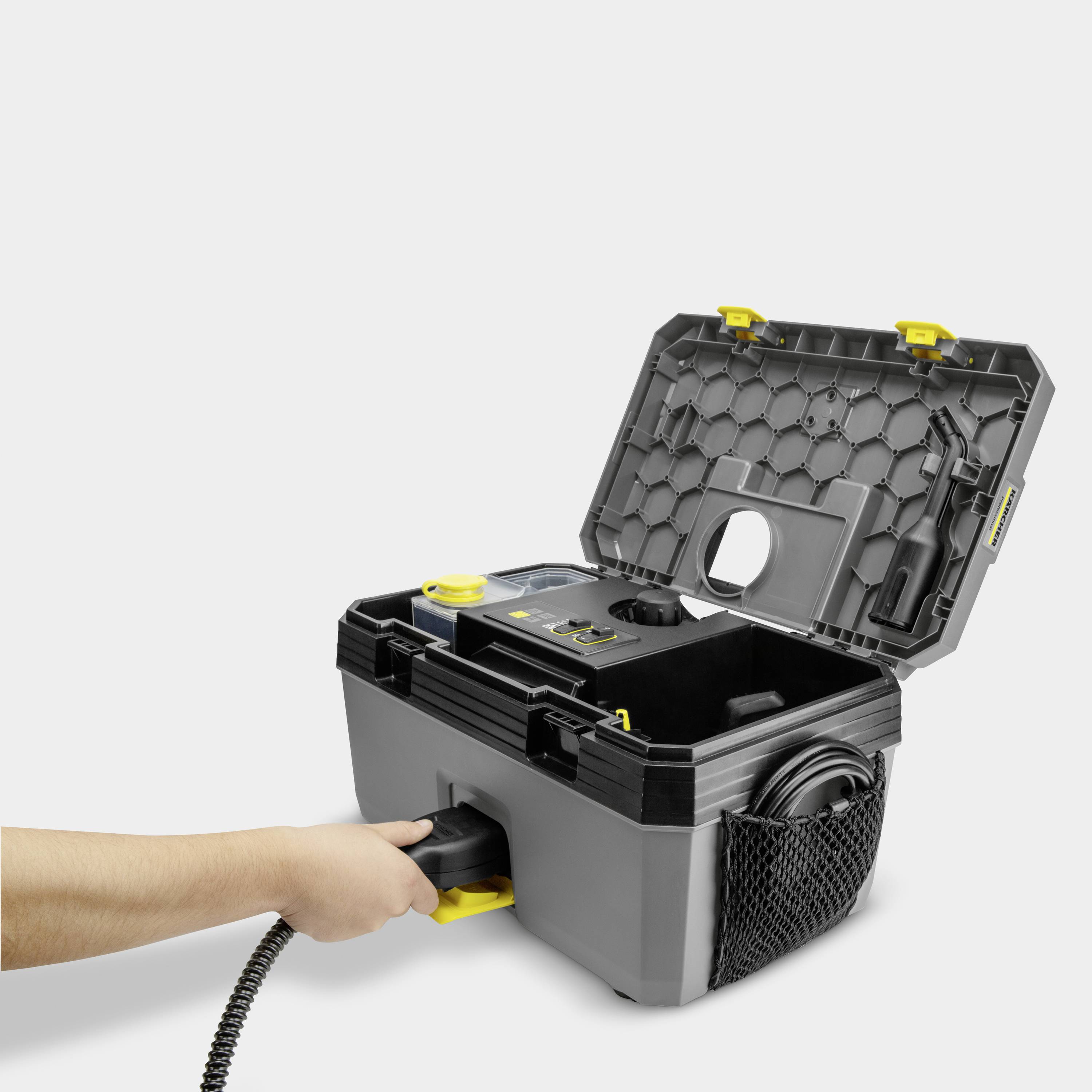 Une personne tient un aspirateur avec le couvercle ouvert. L'aspirateur est gris-noir avec des accents jaunes et possède un insert filtrant rond.