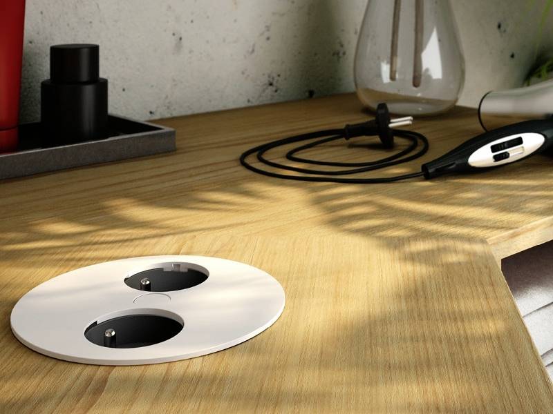 Une table en bois avec un couvre-prise électrique double rond ; à côté se trouvent un sèche-cheveux et une paire d'écouteurs noirs.