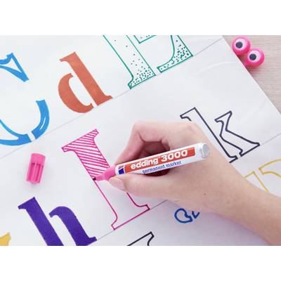 Une main dessine la lettre 'H' en rose avec un marqueur Edding 3000 sur du papier blanc, entourée de lettres colorées.