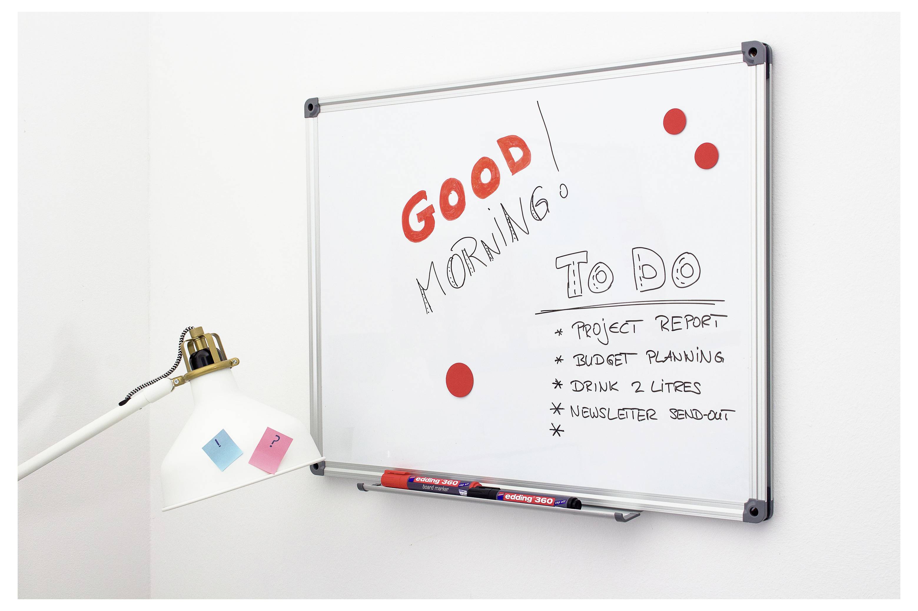 Tableau blanc avec « BON MATIN » et une liste « À FAIRE » : rapport de projet, planification budgétaire, boire 2 litres, envoi d'infolettre ; des notes autocollantes et une lampe à proximité.