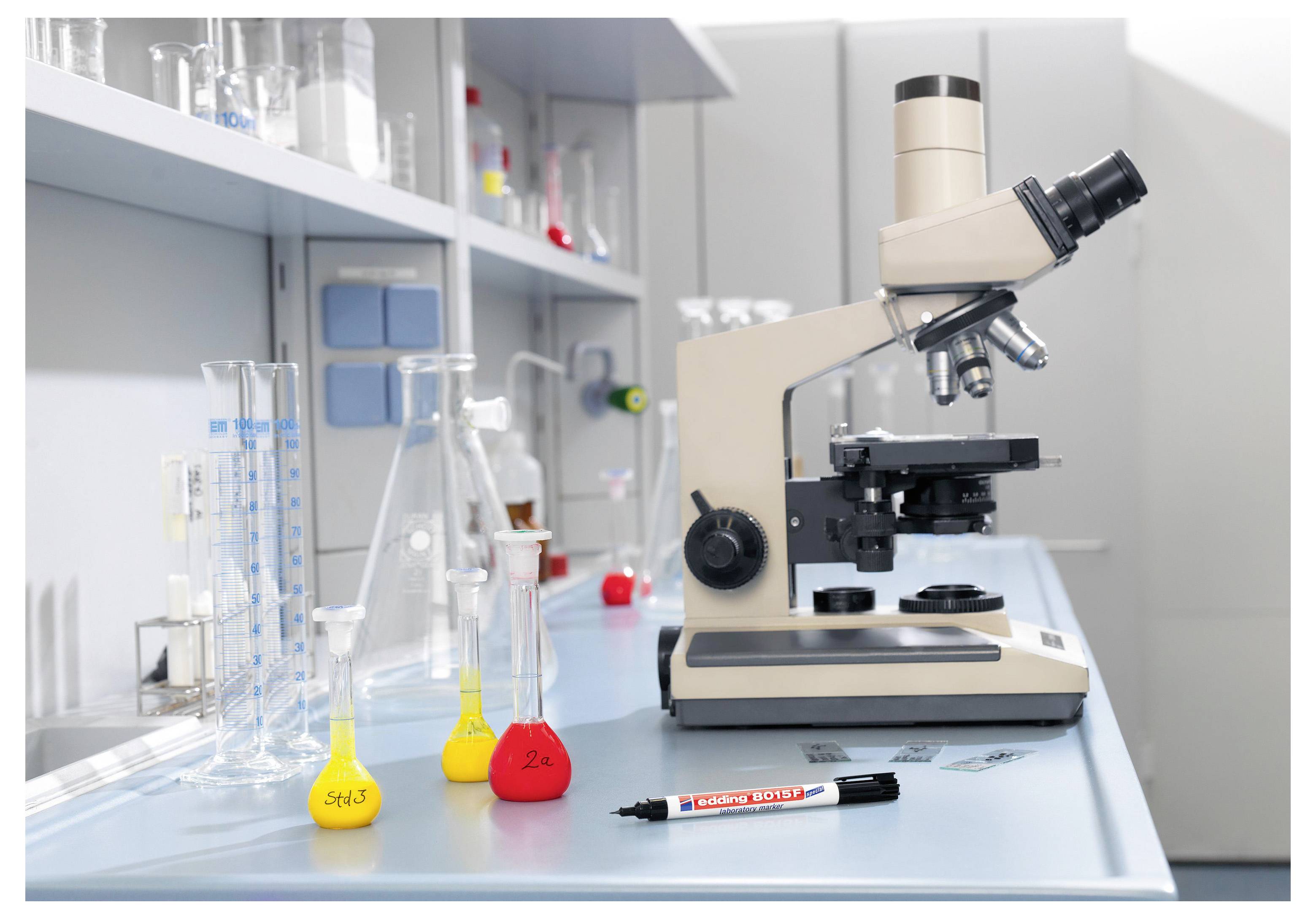 Microscope de laboratoire à côté de béchers en verre et de fioles remplies de liquides colorés sur un plan de travail de laboratoire