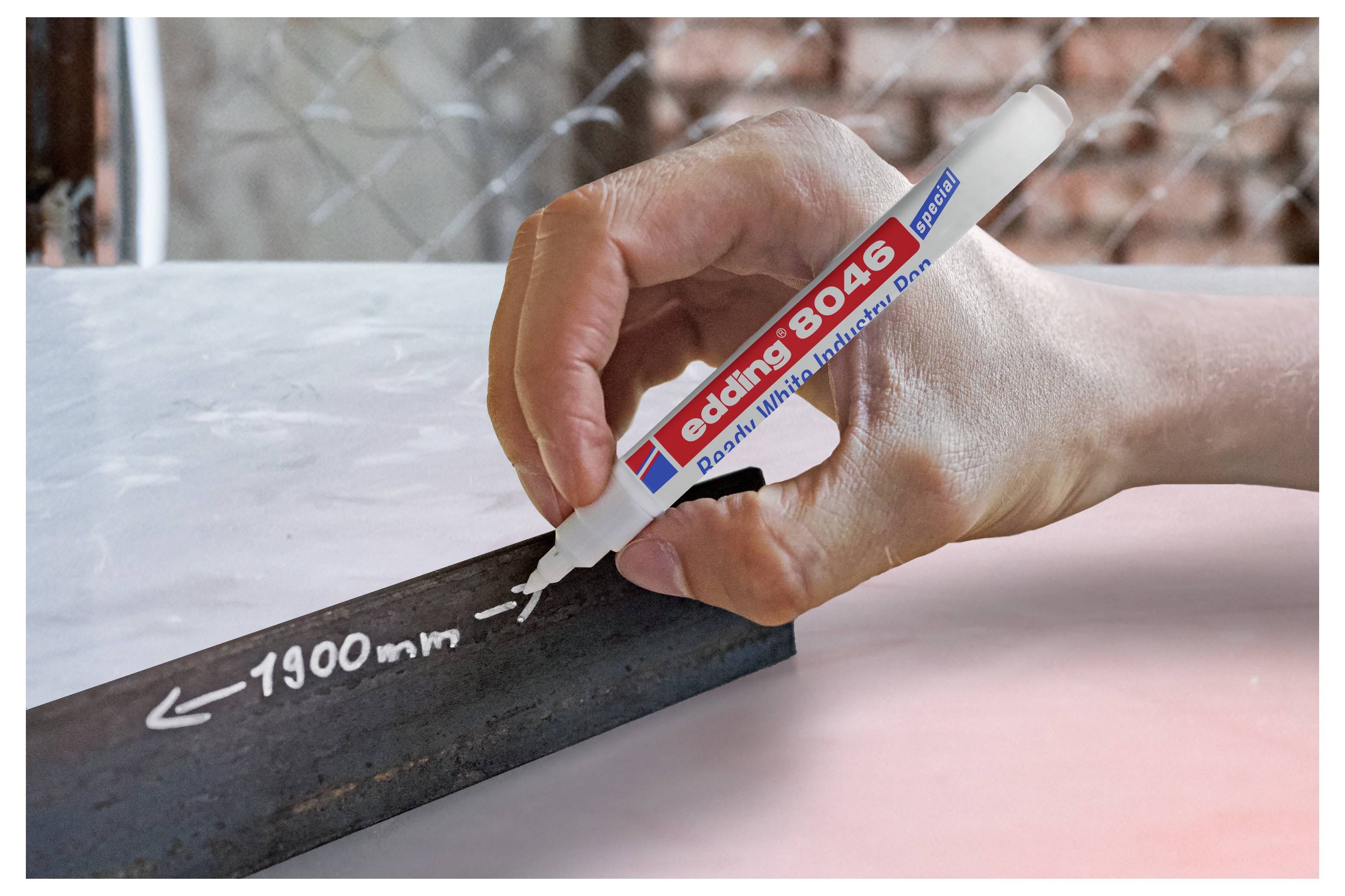Écriture à la main sur une bande noire avec un marqueur de peinture Edding 8046 blanc, étiqueté '1900 mm' avec des flèches, sur une surface claire.