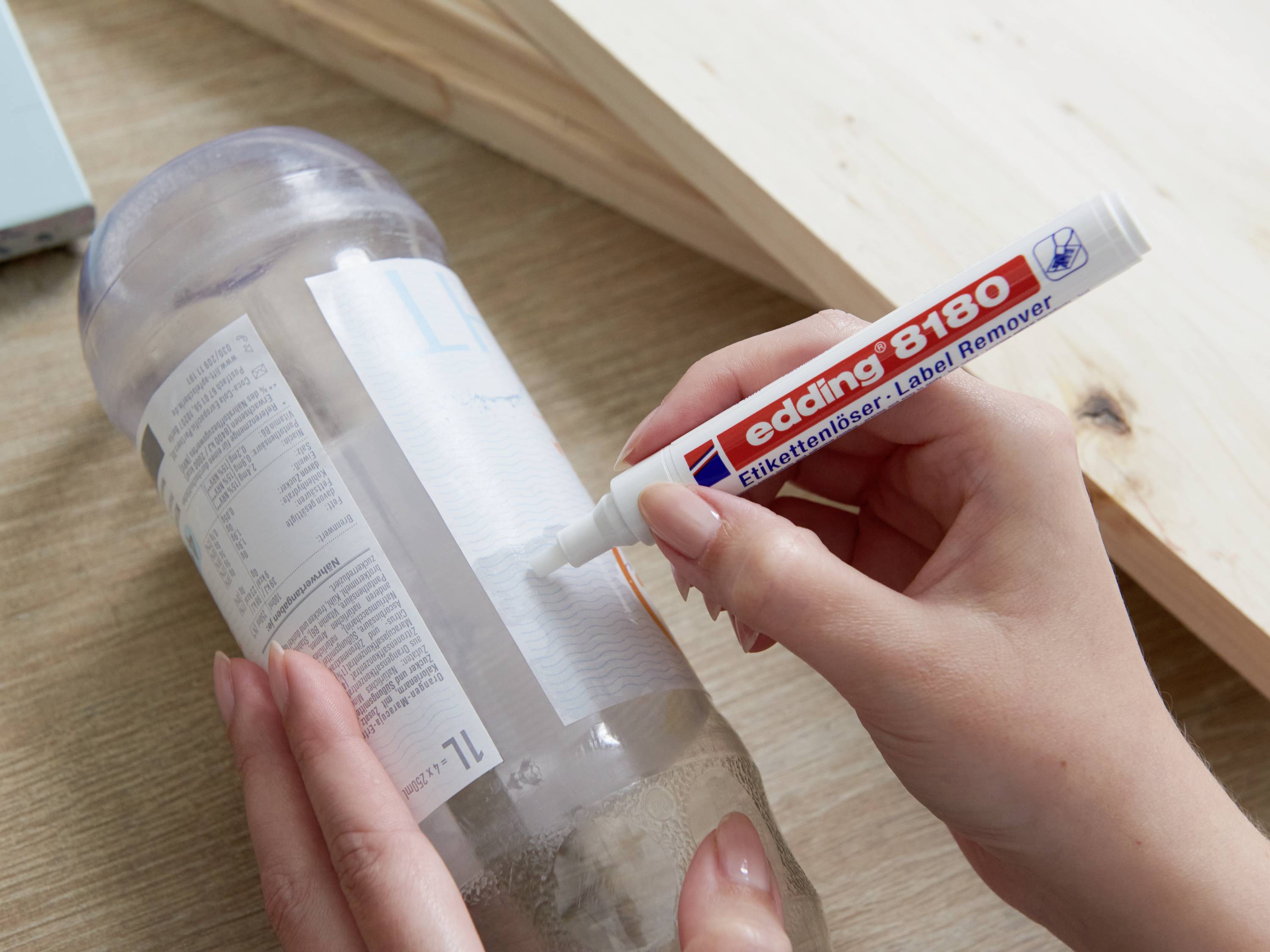 Une personne retire une étiquette d'une bouteille à l'aide d'un stylo dissolvant d'étiquettes 'edding 8180'.