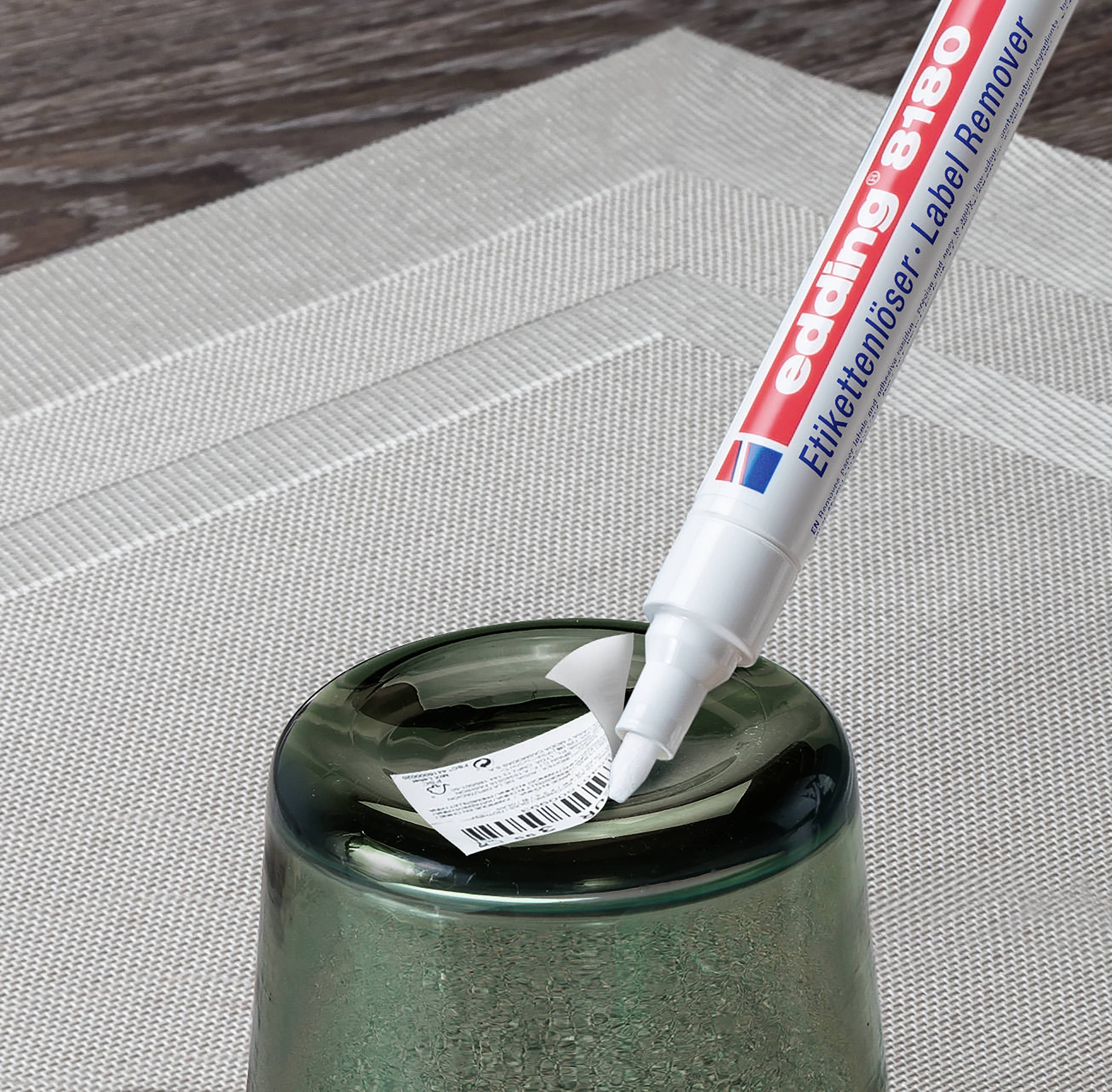 Un stylo blanc portant l'inscription « edding 8400 Label Remover » retire une étiquette d'un objet en verre vert.