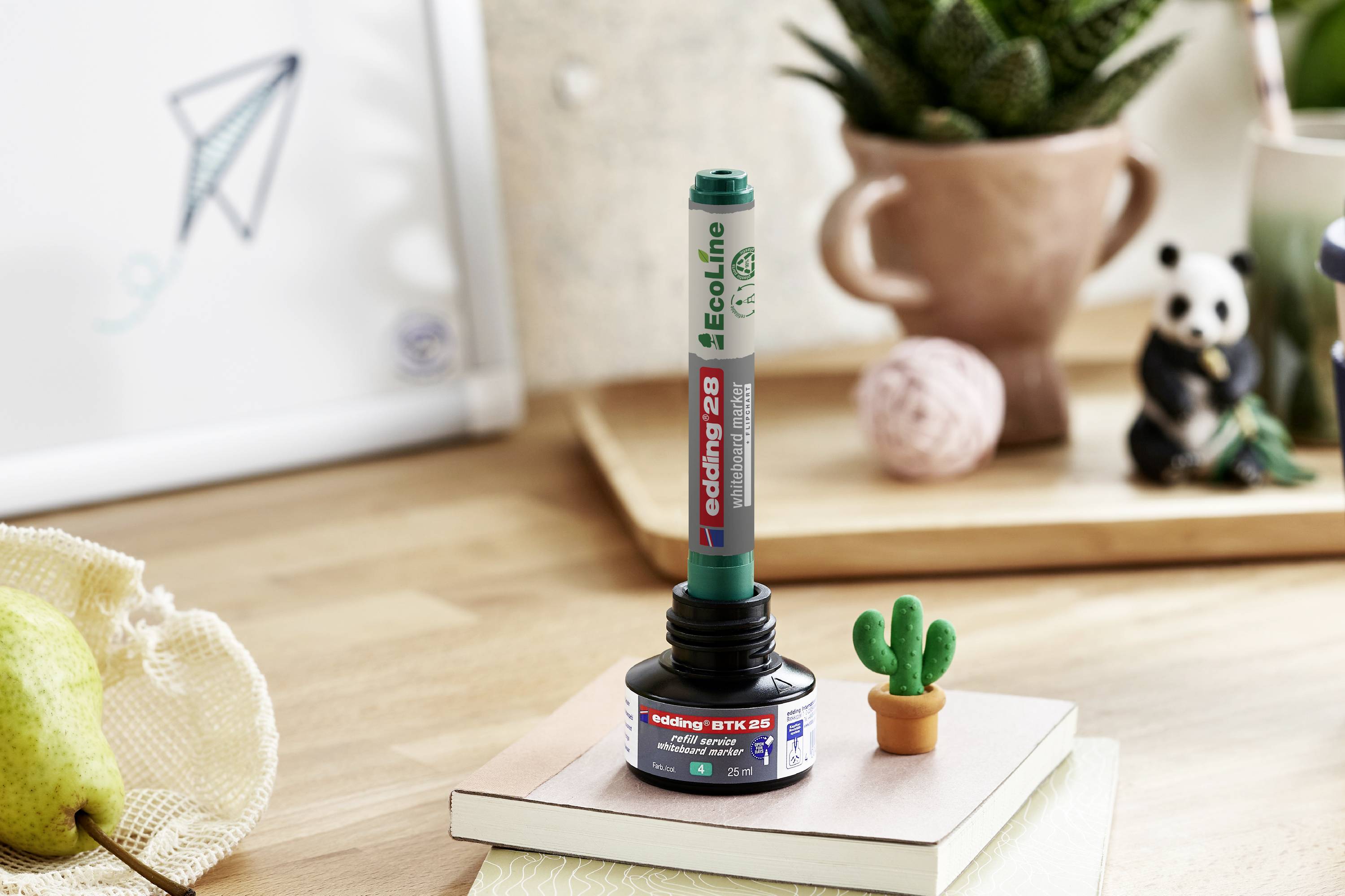Un stylo-feutre vert recharge est posé sur une bouteille d'encre ouverte. En arrière-plan, on aperçoit un petit cactus et un panda décoratif.