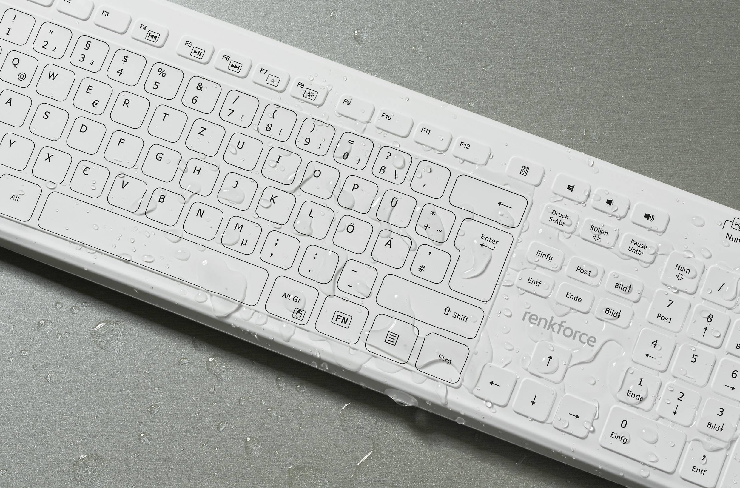 Clavier blanc humide avec des gouttes d'eau sur un fond gris, illustrant une possible vulnérabilité aux dommages causés par l'eau ou la protection contre les éclaboussures.