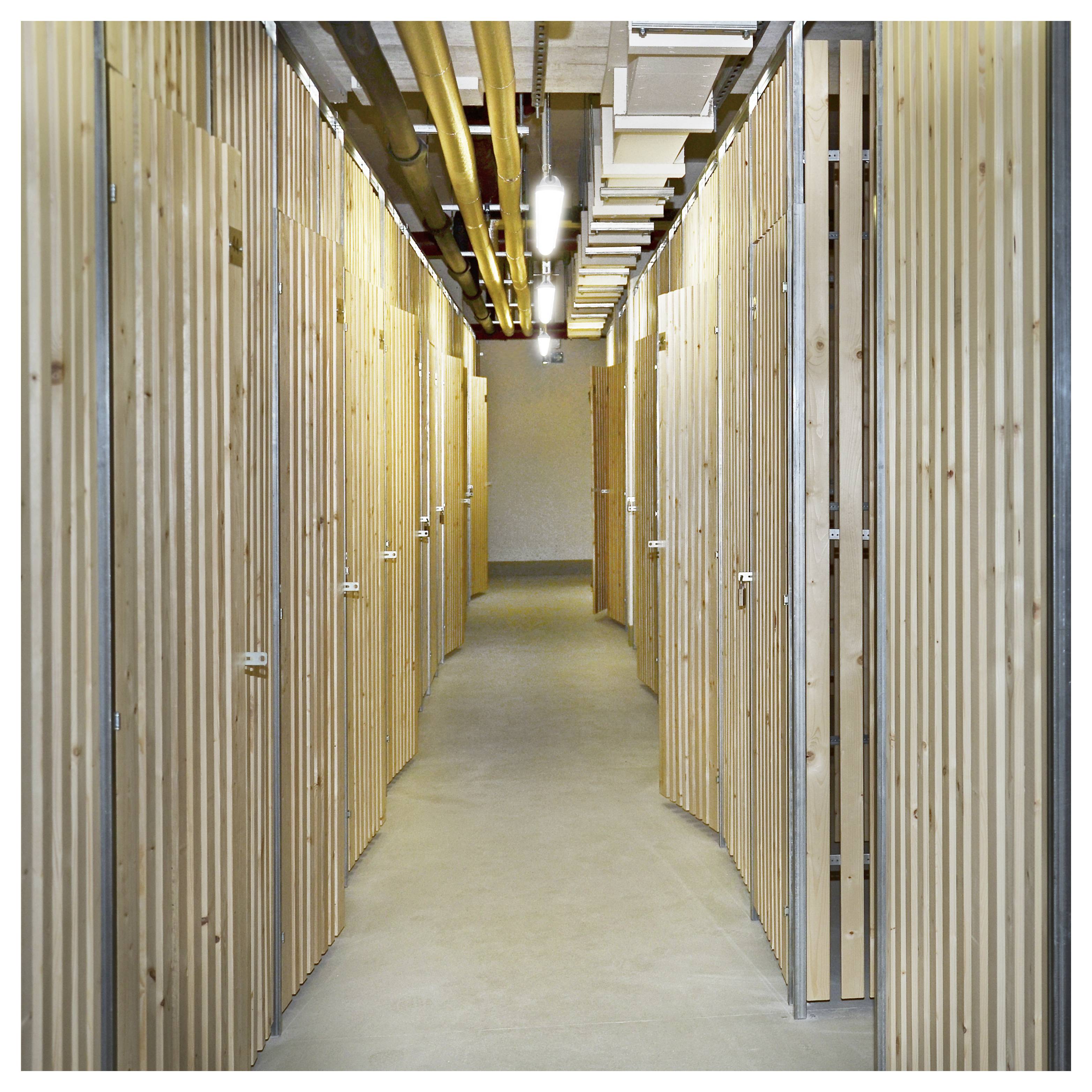 'Un couloir bordé d'unités de rangement en bois, un plafond avec des tuyaux et des lumières apparents, menant à un mur de fond.'