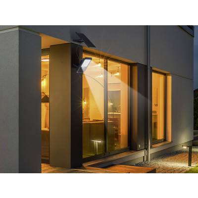 Une lampe solaire illumine la façade moderne d'une maison la nuit. De grandes fenêtres révèlent un salon éclairé.