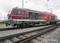 Une locomotive DB Cargo rouge est stationnée sur une voie ferrée. Elle présente un design moderne et est prête pour le transport de marchandises.
