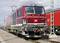 Une locomotive rouge et blanche de la marque ferroviaire allemande 'Siemens Vectron' est stationnée sur des voies ferrées. Des caténaires sont visibles en arrière-plan.
