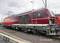 Locomotive DB Cargo rouge sur une voie ferrée, vue de côté, avec caténaire et ciel nuageux en arrière-plan.