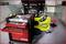 Atelier avec une voiture de course jaune, capot ouvert. Chariot à outils avec tiroirs rouges au premier plan.