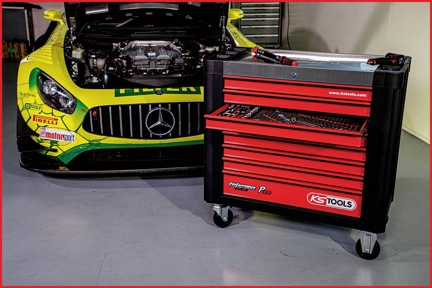 Voiture de sport jaune avec compartiment moteur ouvert, à côté d'un établi roulant rouge, dans un environnement d'atelier.