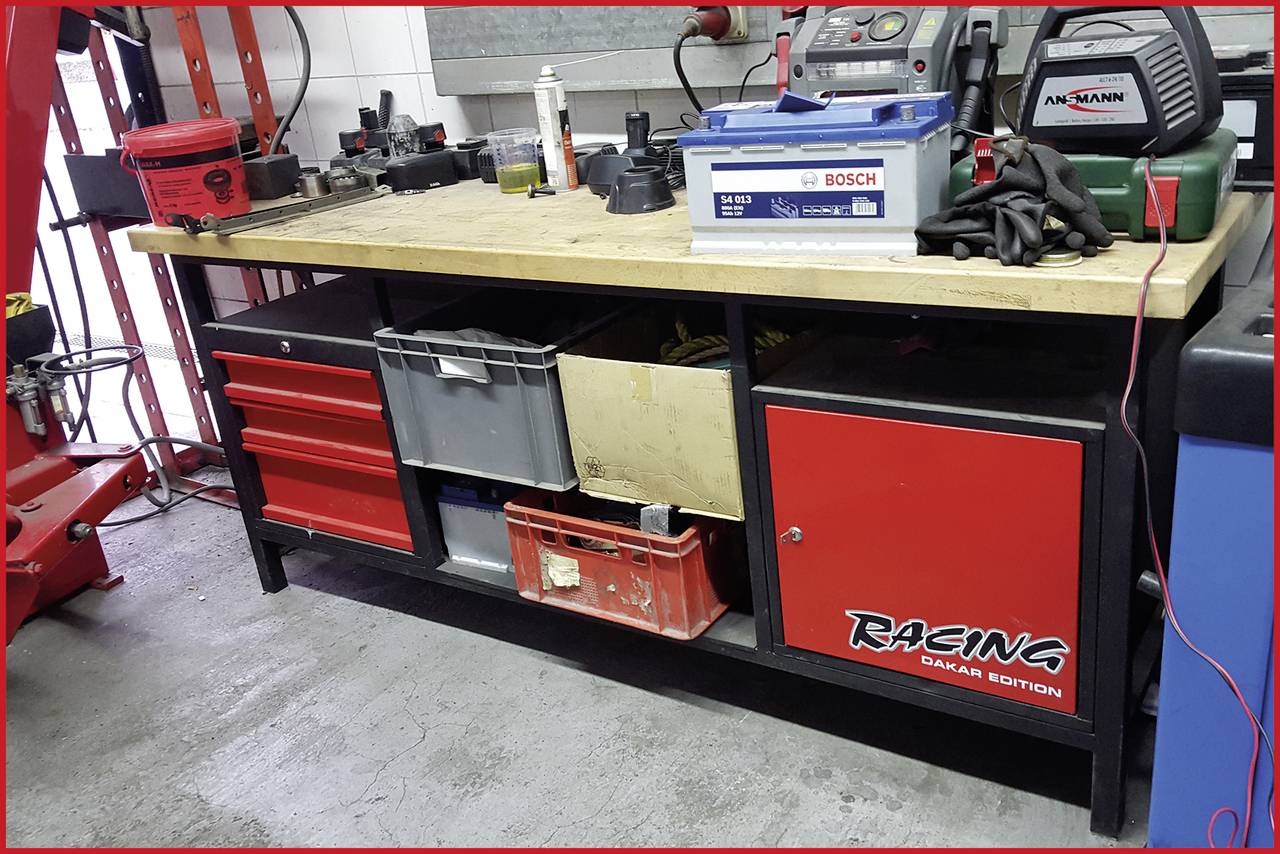 Établi avec tiroirs et étagères, rempli d'outils, d'une batterie et d'équipements. Étiquette 'Racing Dakar Edition'.