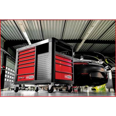 Atelier avec une voiture de sport noire garée dans un garage. Au premier plan, un chariot à outils rouge mobile est stationné.