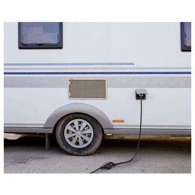 Un camping-car garé sur un chemin de terre avec une prise électrique connectée à son côté, près de la roue, indiquant qu'il est en charge.