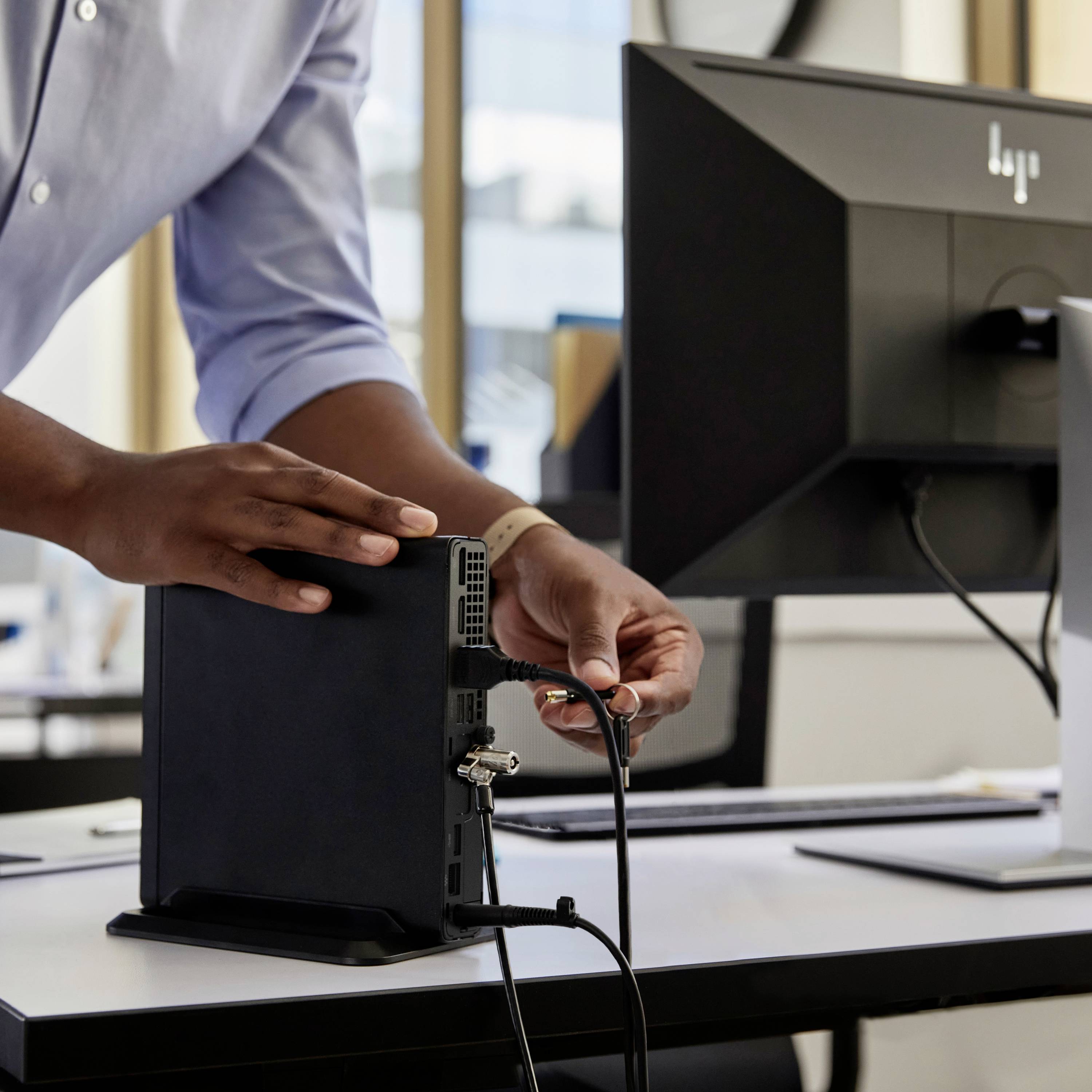 Une personne branche un câble dans un ordinateur de bureau dans un bureau, avec un moniteur visible en arrière-plan.