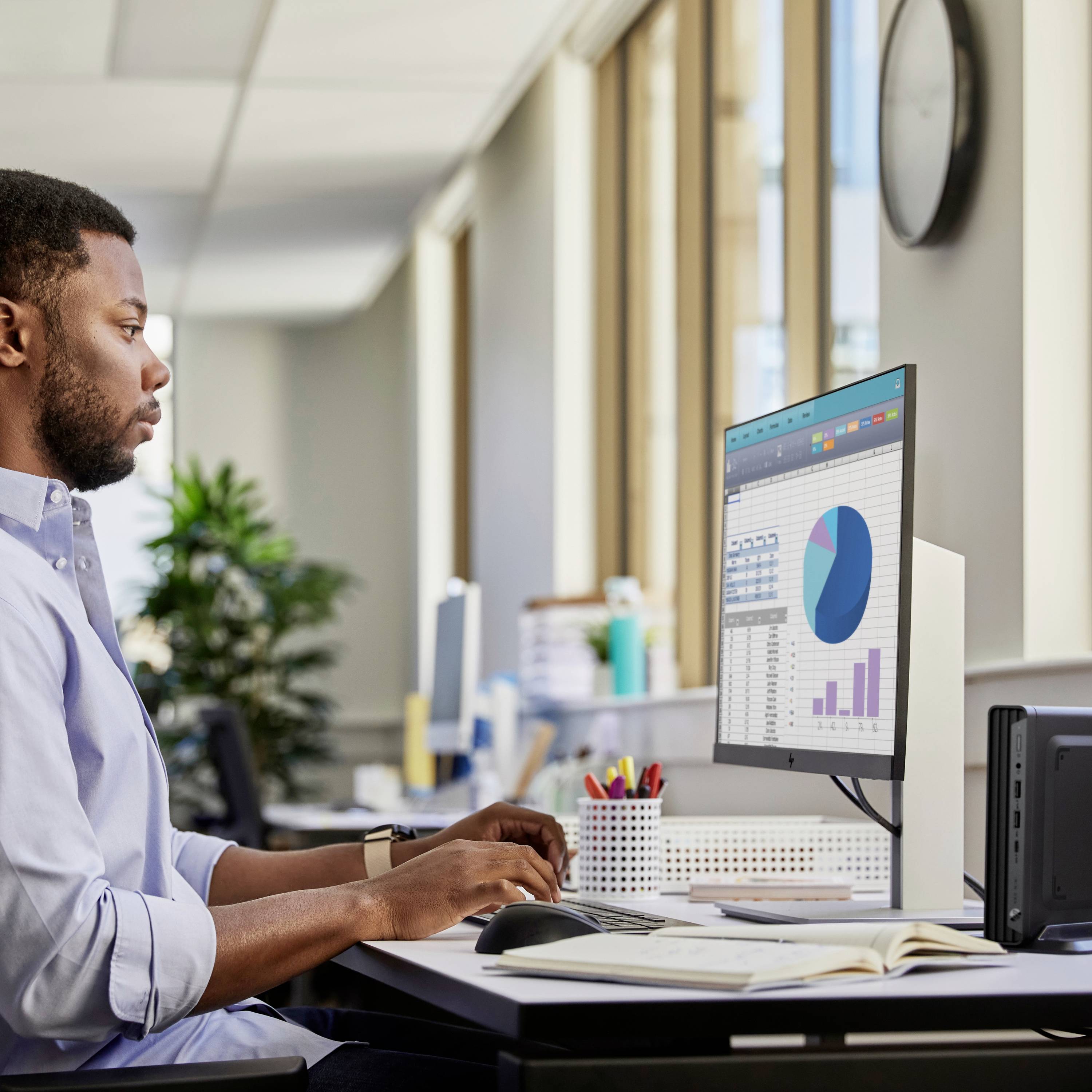 Un homme travaille sur un ordinateur dans un bureau. Sur l'écran, on peut voir des diagrammes avec des barres et un cercle.