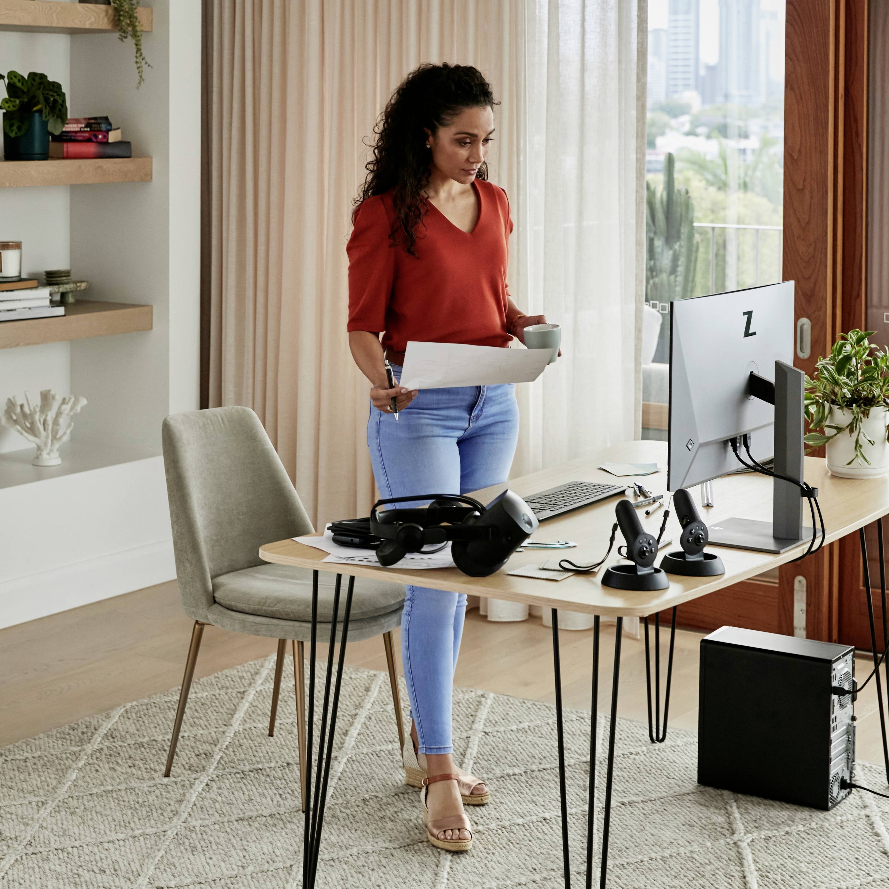 Une femme est debout près d'un bureau, lisant un document. Un ordinateur et un téléphone sont posés sur la table. Un environnement de bureau lumineux et moderne offrant une vue sur la ville.