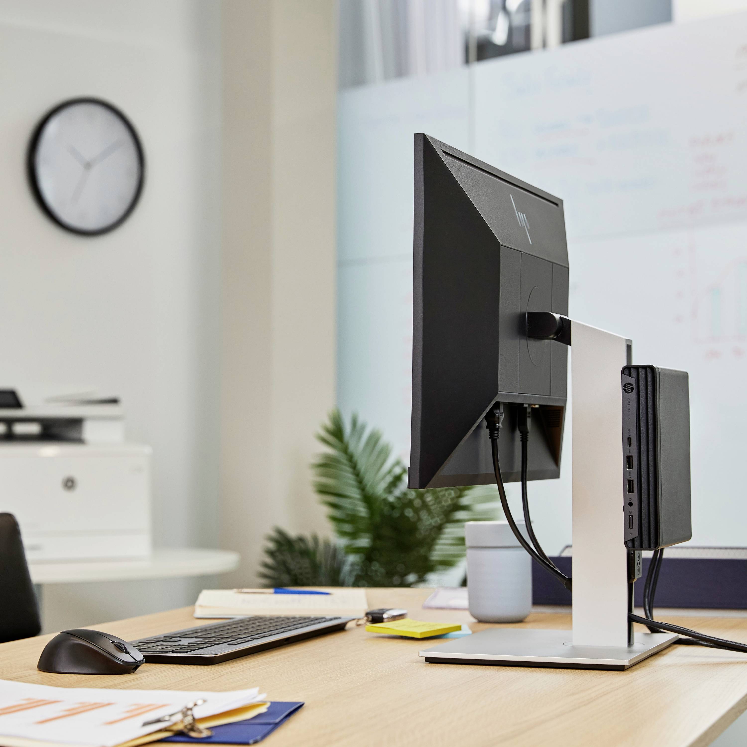 Bureau moderne avec un ordinateur, un écran, un clavier, une souris et des carnets de notes ; en arrière-plan, une horloge et des plantes.