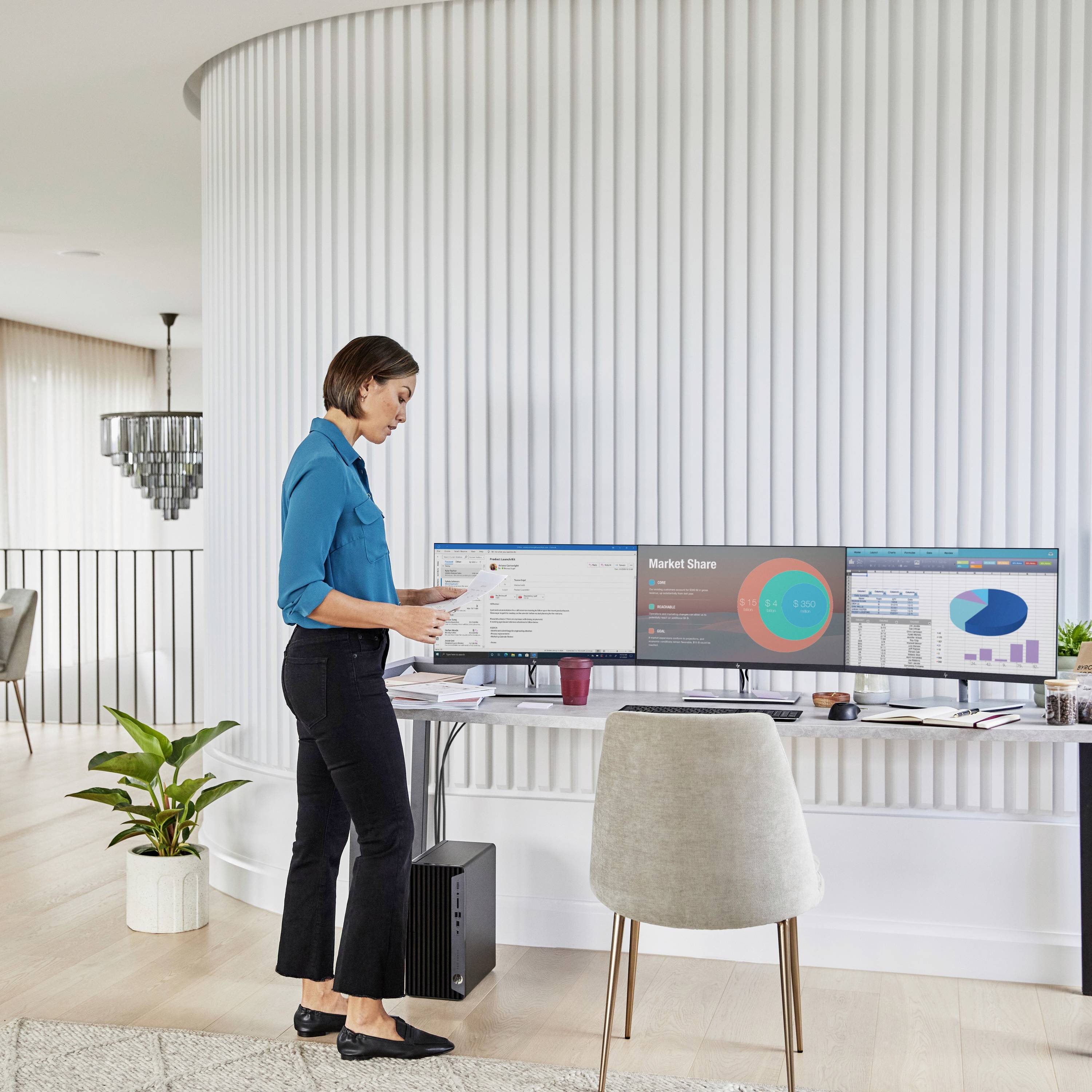 Une femme portant une chemise bleue se tient devant un bureau, regardant deux écrans d'ordinateur affichant des diagrammes de parts de marché et des données.