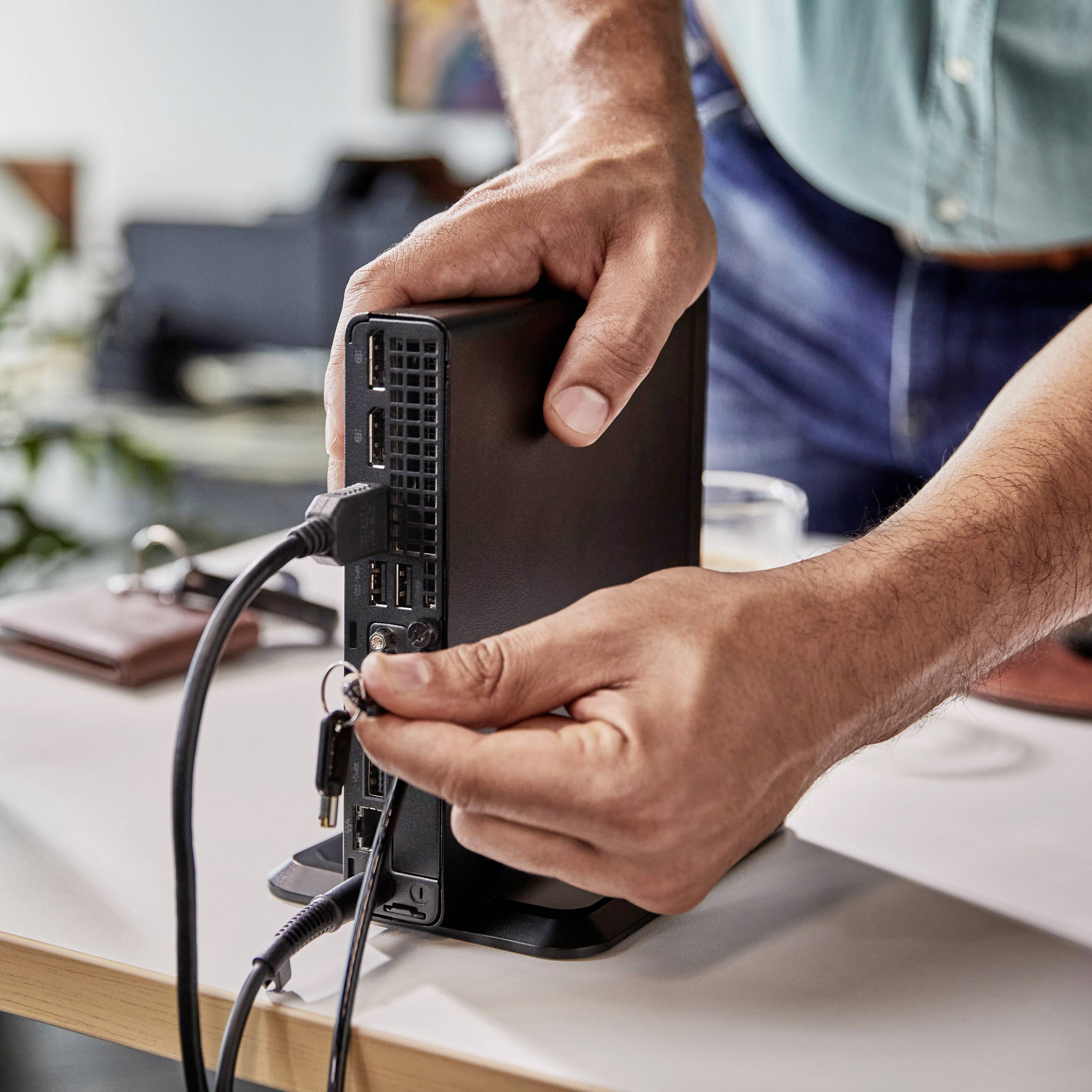 Une personne branche des câbles à l'arrière d'un ordinateur de bureau sur une table pour le configurer ou le connecter.