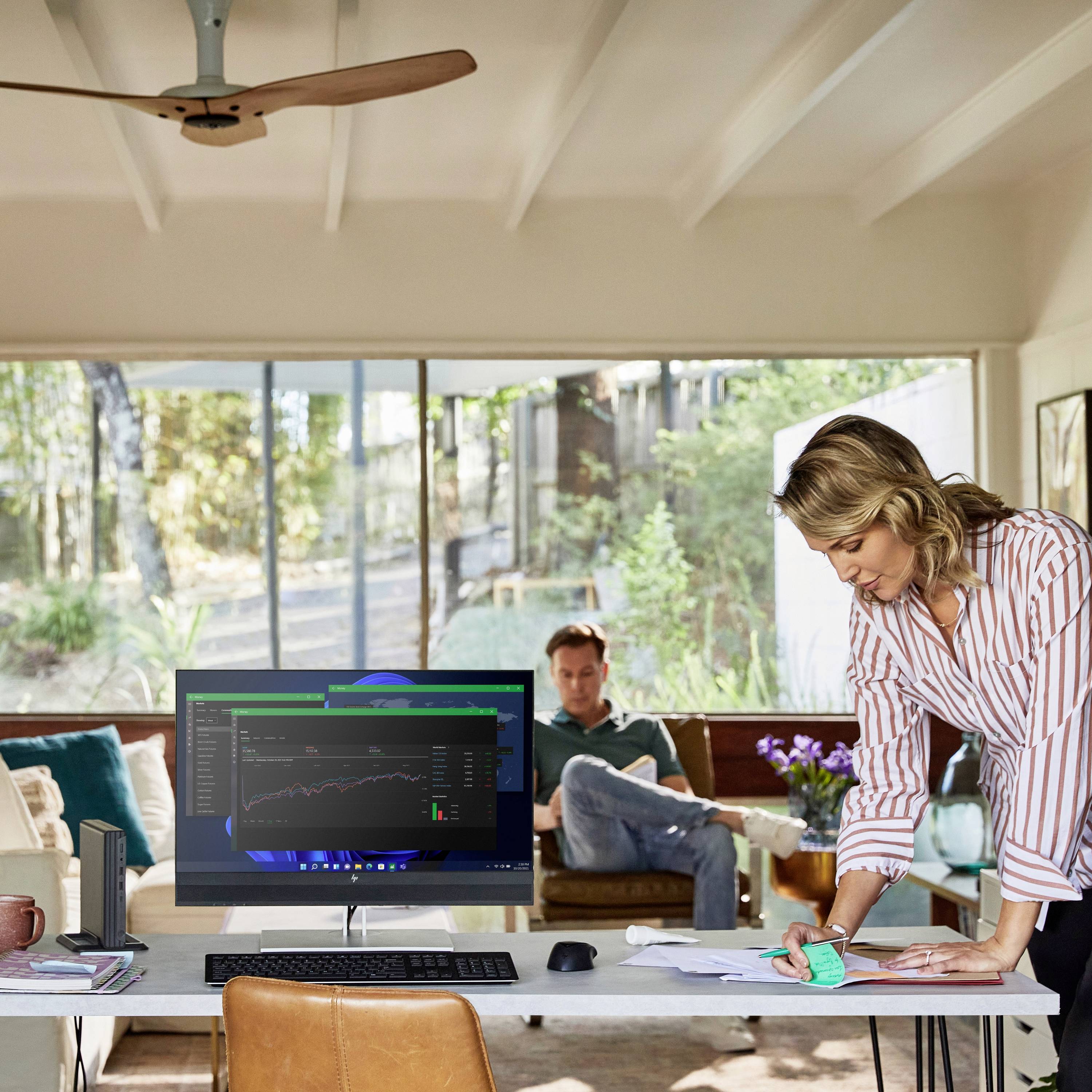 Un bureau avec un moniteur sur une table affichant des diagrammes financiers. Une femme travaille sur un ordinateur portable, tandis qu'un homme est assis en arrière-plan.